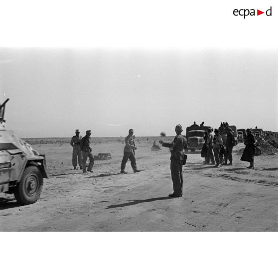 La marche d'une colonne de véhicules est régulée par un Hauptfeldwebel de la Feldgendarmerie, ici un véhicule de reconnaissance Sd.Kfz.222 et des camions.