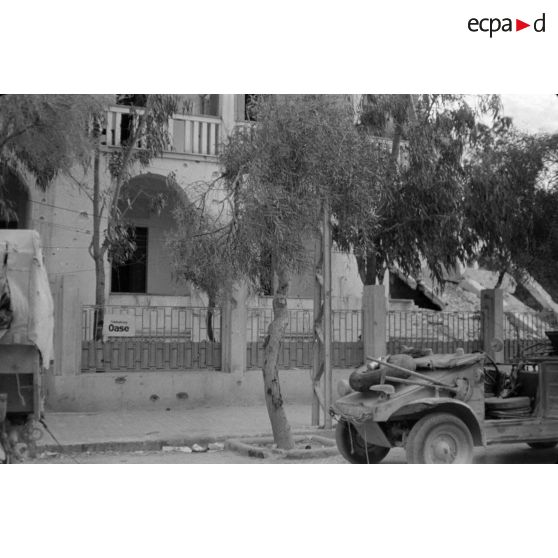 Plusieurs véhicules dont une voiture Kübelwagen garés près du bâtiment servant au journal du front Die Oase.