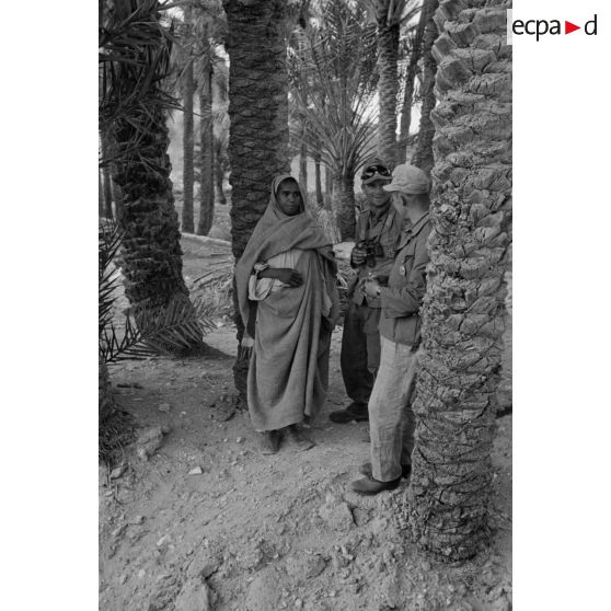 Un lieutenant (Oberleutnant) et un caporal (Gefreiter) discutent avec des habitants du village au milieu des cultures de l'oasis.