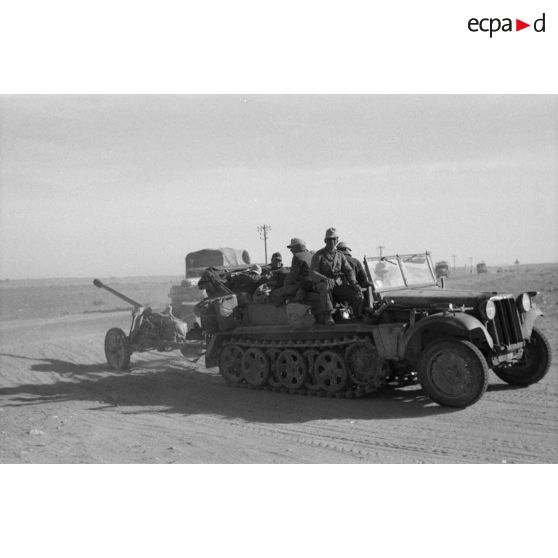 Un convoi de véhicules quitte une piste bordée d'une ligne télégraphique, ici un semi-chenillé Sd.Kfz-10 tractant un canon de 7,5 cm PaK 40.