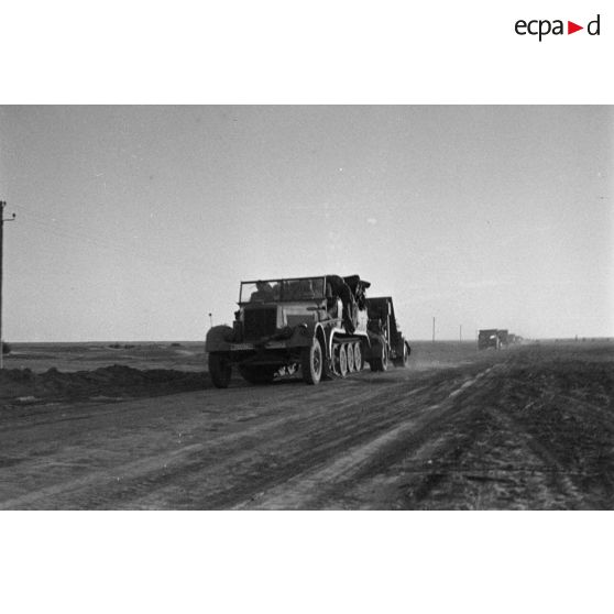 Une unité de FlaK, équipée de véhicules allemands et anglais, se déplace en convoi sur une route, ici un semi-chenillé Sd.Kfz.7 tractant une pièce de 8,8 cm FlaK-18.