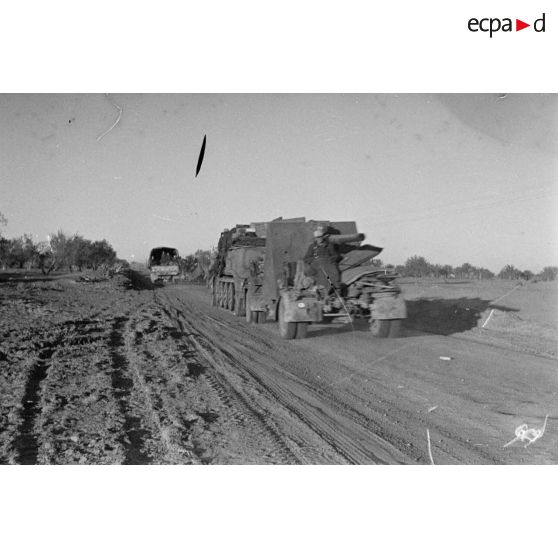 Une unité de FlaK, équipée de véhicules allemands et anglais, se déplace en convoi sur une route, ici un semi-chenillé Sd.Kfz.7 tractant une pièce de 8,8 cm FlaK-18.