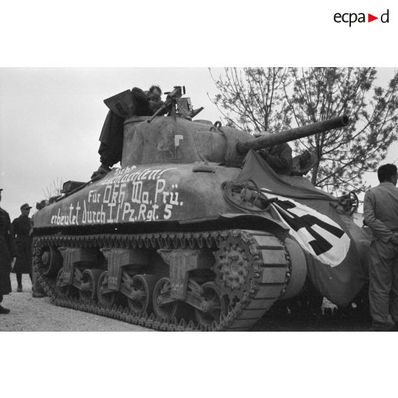 Des soldats allemands entourent un char américain M4A1 recouvert d'un drapeau et d'une inscription.