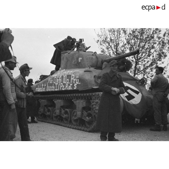 Des soldats allemands entourent un char américain M4A1 recouvert d'un drapeau et d'une inscription.