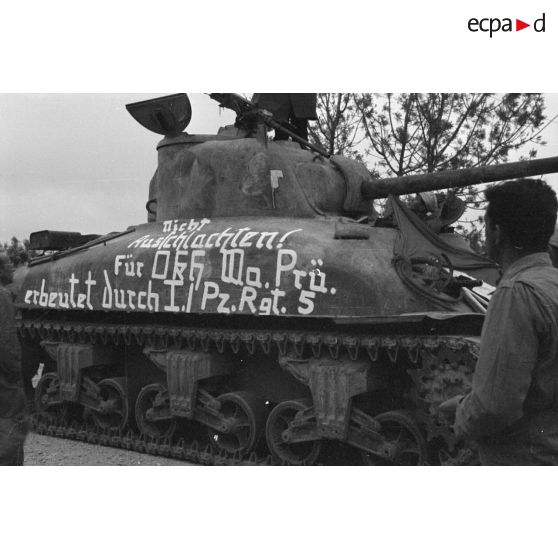 Des soldats allemands entourent un char américain M4A1 recouvert d'un drapeau et d'une inscription.