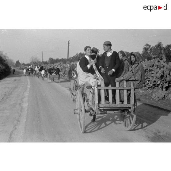 Sur une route, des civils en charrette ou à vélo arborent des drapeaux tunisiens.