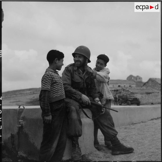 Jeunes garçons algériens jouant avec la barbe d'un soldat de la 57e compagnie de transmissions de la 7e DMR (division mécanique rapide) au sud de Sétif.