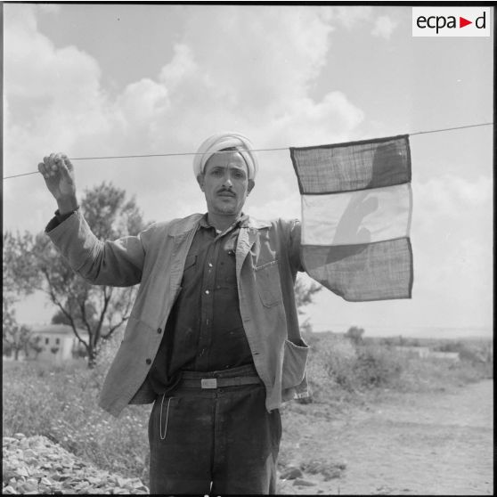 Ouvrier algérien accrochant un drapeau français pour l'inauguration des nouvelles habitations du village de Mondovi (Dréan).