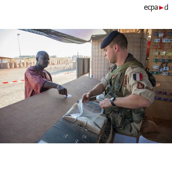 Le sergent-chef Benjamin, chef du poste de sécurité, réceptionne la pièce d'identité d'un employé civil à l'entrée du camp de Bamako, au Mali.