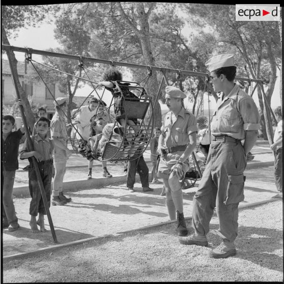 Des soldats du 18e régiment de chasseurs parachutistes(RCP) regardant des enfants s'amuser sur des balançoires.