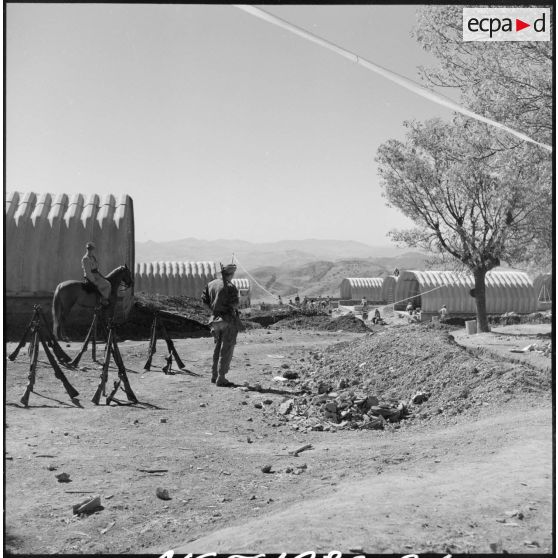 Un garde-faisceau de la 3/131e régiment d'infanterie (RI) surveille les fusils de ces camarades qui construisent des baraquements.