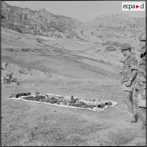 Le colonel Meyer, commandant le 1er régiment de chasseurs parachutistes (RCP), devant l'arsenal pris aux rebelles, dans le paysage du Djebel.