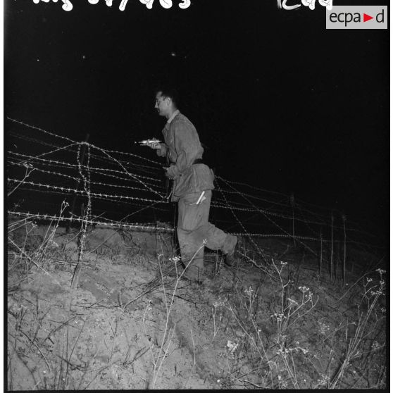 Patrouille de nuit dans le réseau électrifié. Le sous-lieutenant Coppola de la 9ème compagnie du 3/60ème régiment d'infanterie (RI) vérifie les fils barbelés.