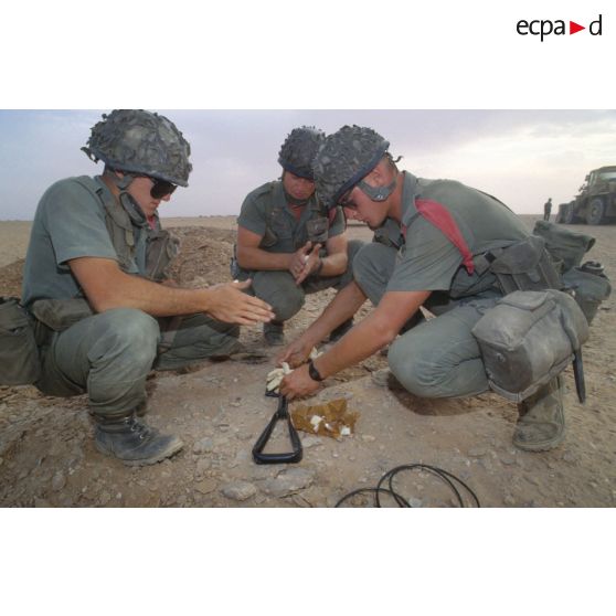 Des soldats du génie manipulent des pains de plastic à enfouir dans le sable et des mèches lentes pour préparer un fourneau d'explosion lors d'un entraînement au tir à l'explosif.