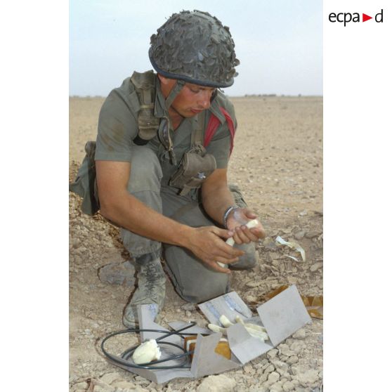 Un soldat du génie manipule des pains de plastic à enfouir dans le sable et des mèches lentes pour préparer un fourneau d'explosion lors d'un entraînement au tir à l'explosif.