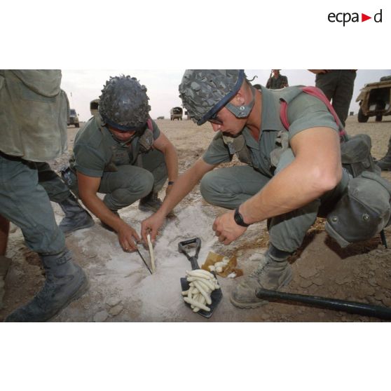 Des soldats du génie enfouissent des pains de plastic dans le sable et posent des mèches lentes pour préparer un fourneau d'explosion lors d'un entraînement au tir à l'explosif.