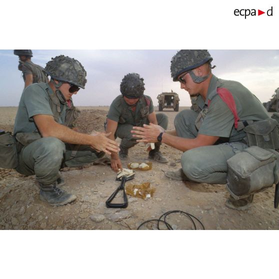 Des soldats du génie manipulent des pains de plastic à enfouir dans le sable avec des mèches lentes pour préparer un fourneau d'explosion lors d'un entraînement au tir à l'explosif.