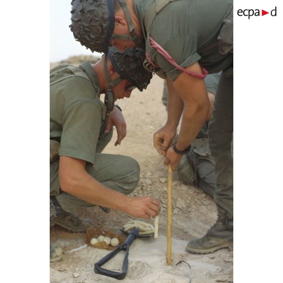 Des soldats du génie enfouissent des pains de plastic dans le sable et posent des mèches lentes pour préparer un fourneau d'explosion lors d'un entraînement au tir à l'explosif.