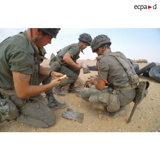 Des soldats du génie manipulent des pains de plastic à enfouir dans le sable avec des mèches lentes pour préparer un fourneau d'explosion lors d'un entraînement au tir à l'explosif.