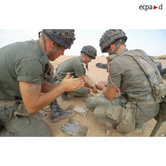 Des soldats du génie manipulent des pains de plastic à enfouir dans le sable avec des mèches lentes pour préparer un fourneau d'explosion lors d'un entraînement au tir à l'explosif.