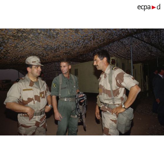 Le général de brigade Raymond Germanos, chef du SIRPA (Service d'information et de relations publiques des Armées), un lieutenant et un sergent-chef photographe de l'équipe de l'ECPA (Etablissement cinématographique et photographique des Armées) passent le soir de Noël sur le campement du 2e REI.