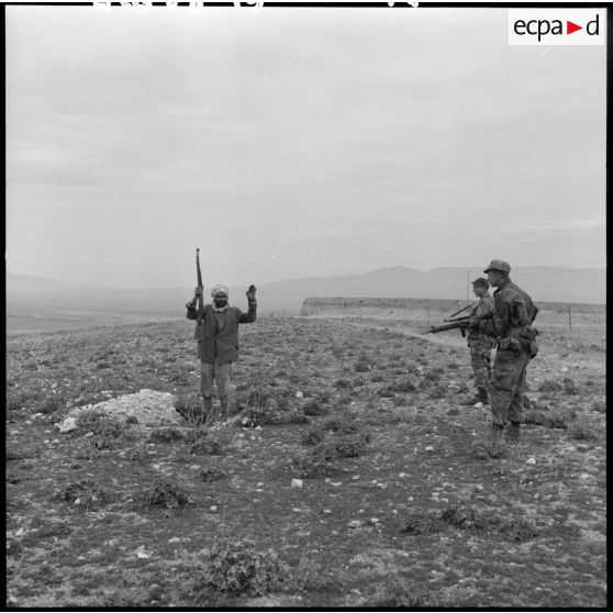 Un homme, mains en l’air et tenant un fusil, se rend devant deux soldats armés lors d’une opération héliportée sur le djebel Tarf.