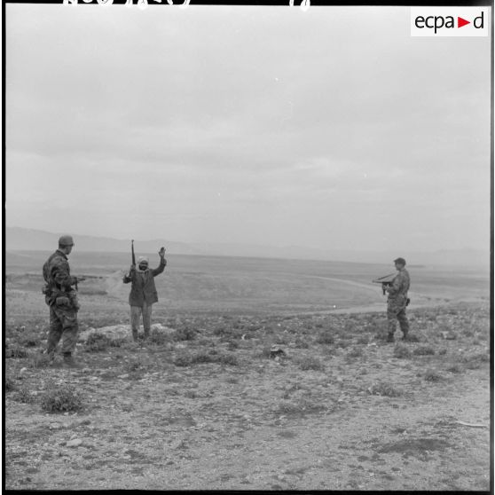 Un homme, mains en l’air et tenant un fusil, se rend devant deux soldats armés lors d’une opération héliportée sur le djebel Tarf.