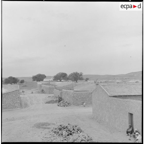 Des hommes et des enfants devant des maisons.