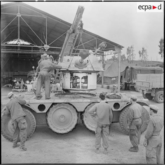 Mécaniciens supervisant la pose par une grue du haut d'un EBR (engin blindé de reconnaissance).