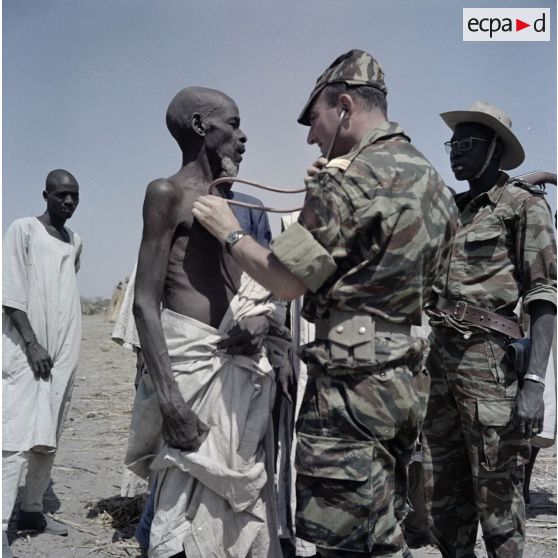 Un capitaine médecin ausculte un paysan malade, accompagné d'un gendarme tchadien.