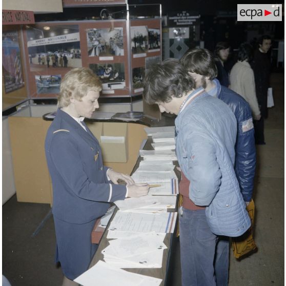 Une hôtesse renseigne des étudiants sur un espace du stand de l'exposition Jeunesse 1976, dans l'ancienne gare à Paris.