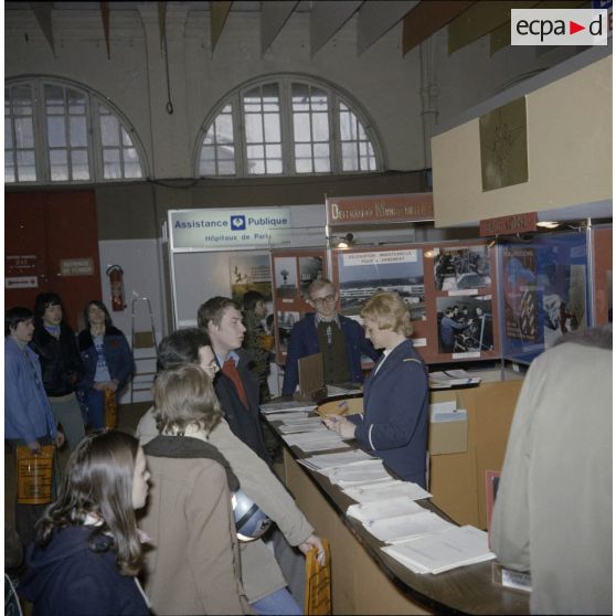 Une hôtesse accueille des étudiants sur l'espace du stand de l'exposition Jeunesse 1976, dans l'ancienne gare de la Bastille à Paris.