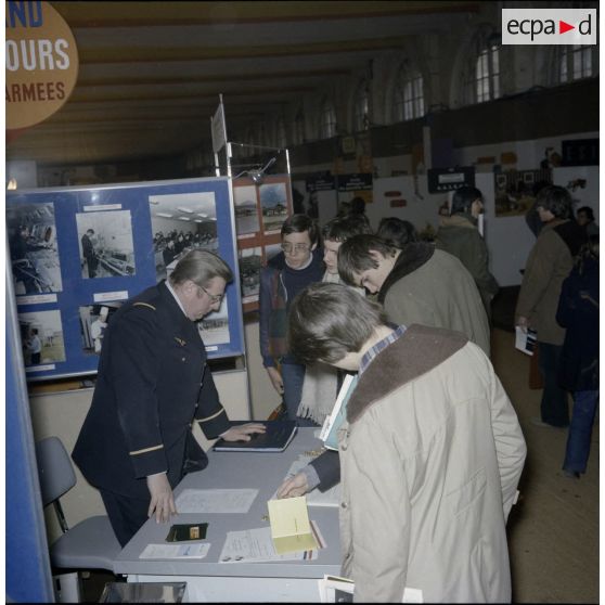 Un homme accueille des étudiants sur un espace du stand de l'exposition Jeunesse 1976, dans l'ancienne gare de la Bastille.