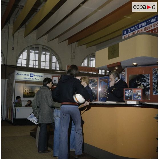 Une femme et un homme accueillent des étudiants sur le stand de l'exposition Jeunesse 1976, dans l'ancienne gare de la Bastille à Paris.