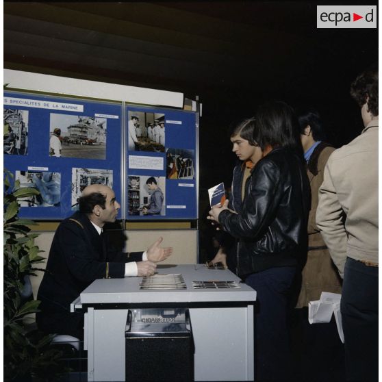 Un homme accueille des étudiants sur un espace du stand de l'exposition Jeunesse 1976, dans l'ancienne gare de la Bastille à Paris.