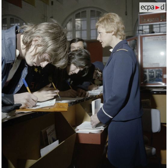 Une hôtesse accueille des étudiants sur un espace de l'exposition Jeunesse 1976, dans l'ancienne gare de la Bastille à Paris.