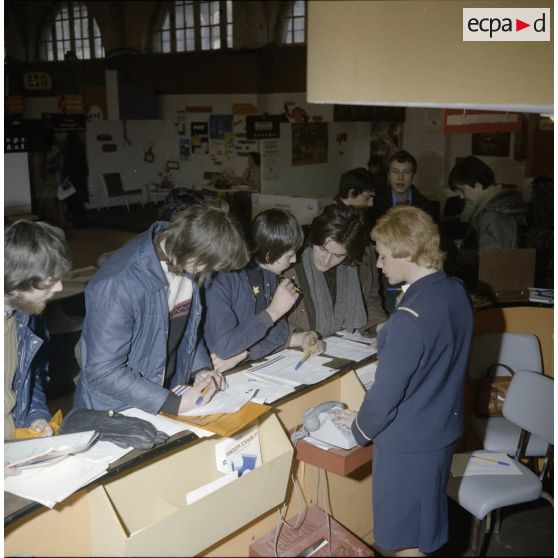 Une hôtesse accueille des étudiants sur un espace du stand de l'exposition Jeunesse 1976, dans l'ancienne gare de la Bastille.