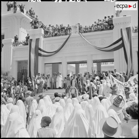 Des femmes face à la mairie écoutent le discours du général Massu, qu'il prononce depuis la terrasse de la Mairie, derrière le portrait du général de Gaulle.