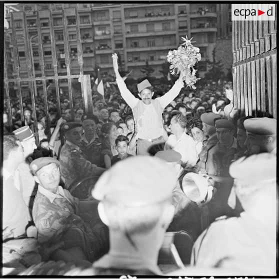 Un homme en costume traditionnel, tenant un bouquet de fleurs, entre au gouvernement de l'Algérie debout sur le capot d'une voiture, à Alger.