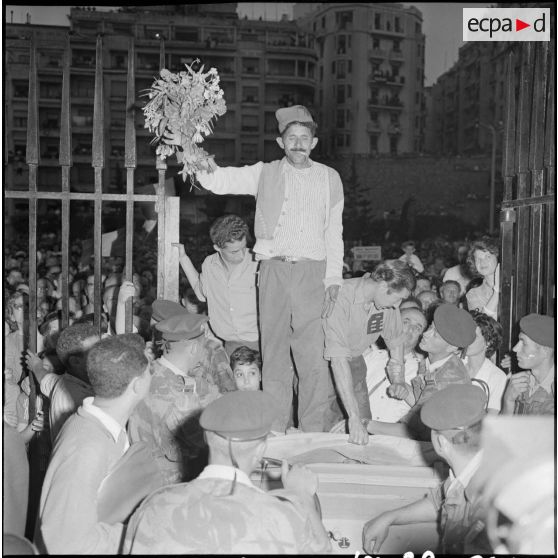 Un homme en costume traditionnel, tenant un bouquet de fleurs, entre au gouvernement de l'Algérie debout sur le capot d'une voiture, à Alger.