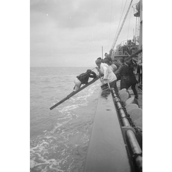 Depuis un dragueur de mines (Minensuchboot), un marin allemand récupère une bouée de sauvetage tombée à la mer.