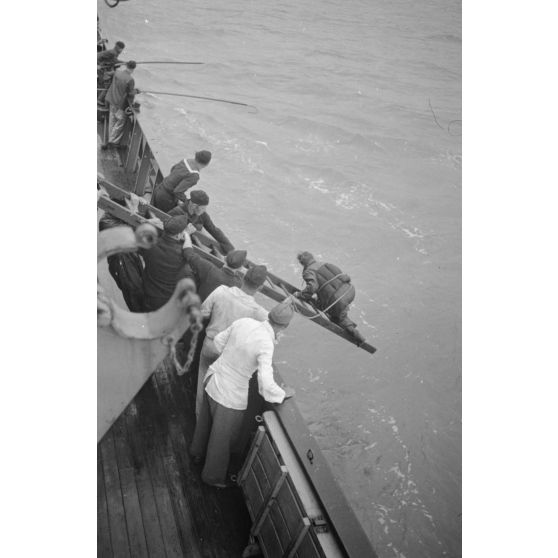 Depuis un dragueur de mines (Minensuchboot), un marin allemand récupère une bouée de sauvetage tombée à la mer.