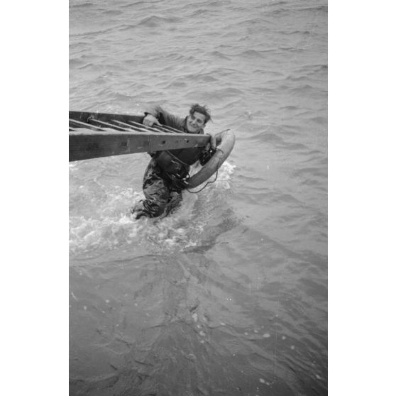 Depuis un dragueur de mines (Minensuchboot), un marin allemand récupère une bouée de sauvetage tombée à la mer.