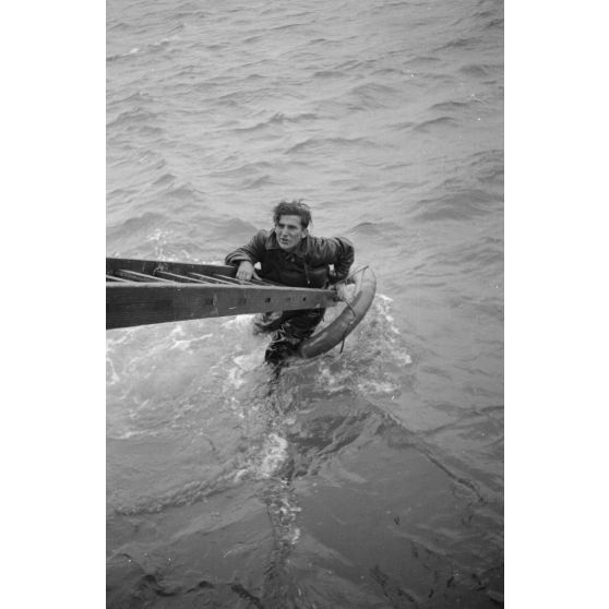 Depuis un dragueur de mines (Minensuchboot), un marin allemand récupère une bouée de sauvetage tombée à la mer.