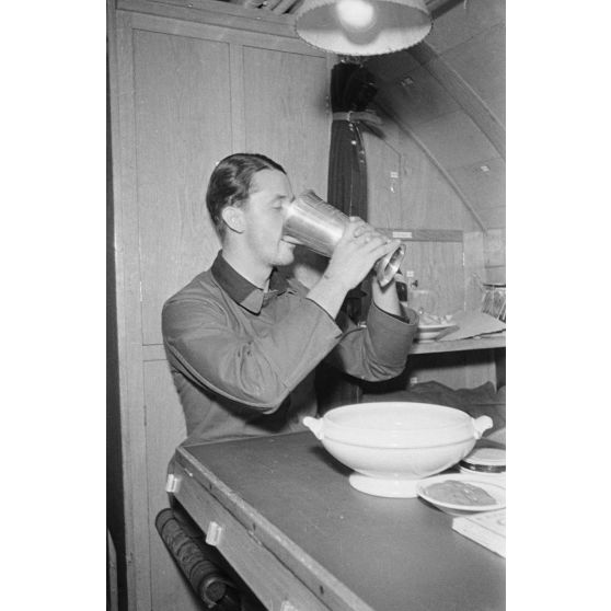 A la table réservée aux officiers du bord, le Kapitänleutnant Rolf Mützelburg commandant du sous-marin U-203, boit un liquide contenu dans un Ehrenpokal.