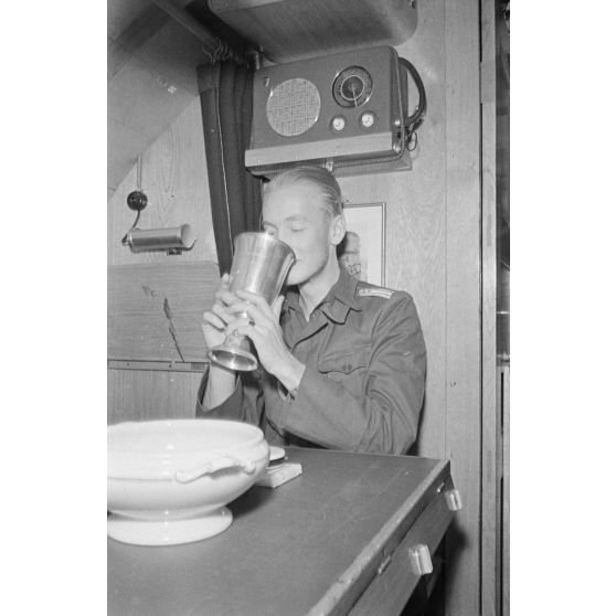 A la table réservée aux officiers du bord, un officier du sous-main U-boot U-203 boit un liquide contenu dans un Ehrenpokal.