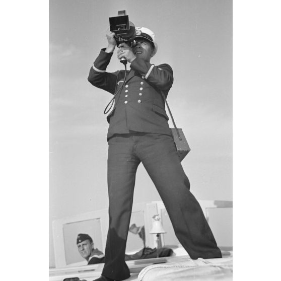 A bord d'un navire léger, non loin du port de Saint-Nazaire, un cameraman équipé de son Arriflex 35 mm filme le retour du sous-marin U-552 (non visible).