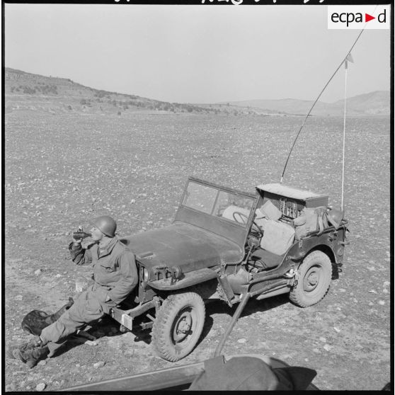 Opération Saïda n°1. Un soldat boit, assis devant une une jeep équipée d'une radio de type SCR-608, avec un chien assis à ses côtés.