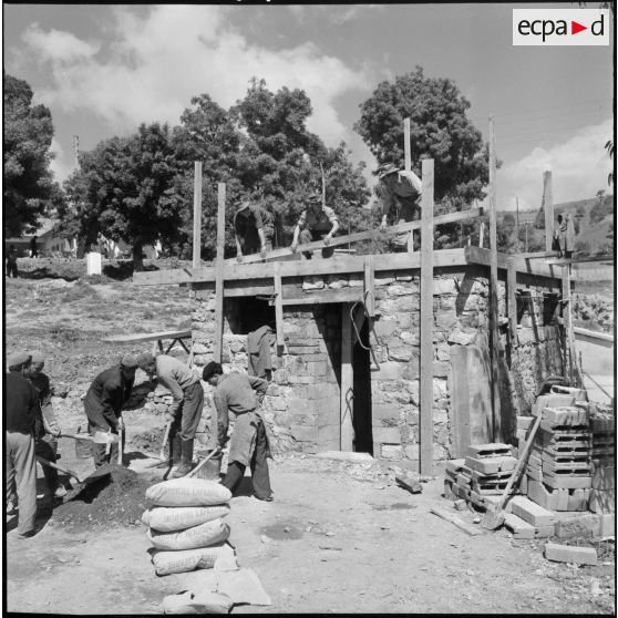 Un soldat maçon à Boudjima construit, avec l'aide de deux camarades et de quelques manoeuvres kabyles, une installation de douche pour son unité.