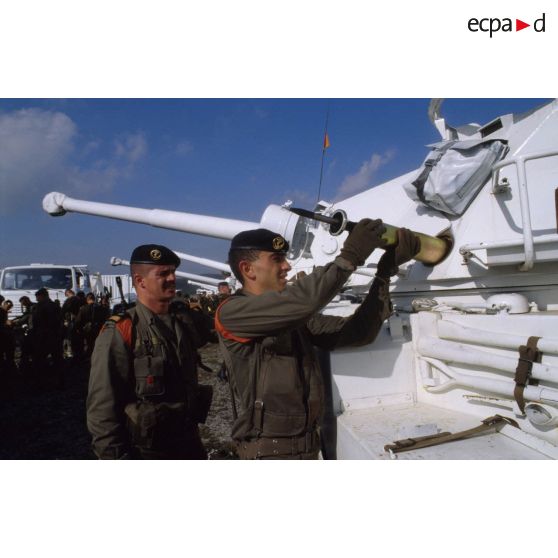 Capitaine observant un marsouin du 1er régiment d'infanterie de marine (1er Rima) chargeant un obus 90 mm dans un véhicule blindé à roues ERC-90 Sagaie aux couleurs de l'ONU.